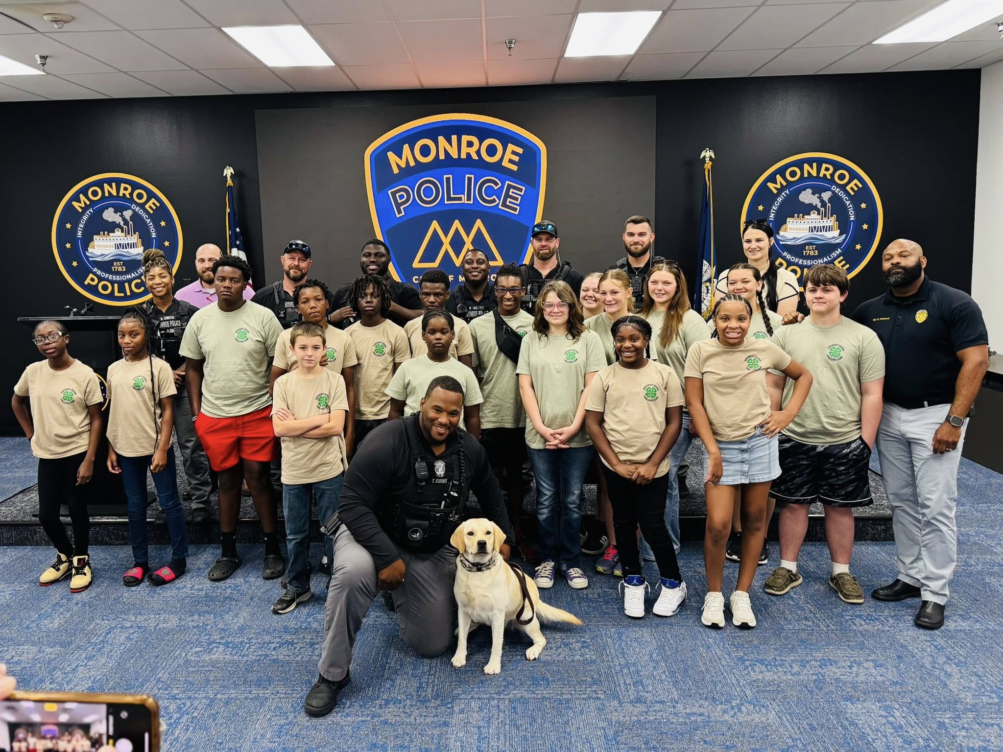 A group of police officers, kids, and a police dog posing for a picture.